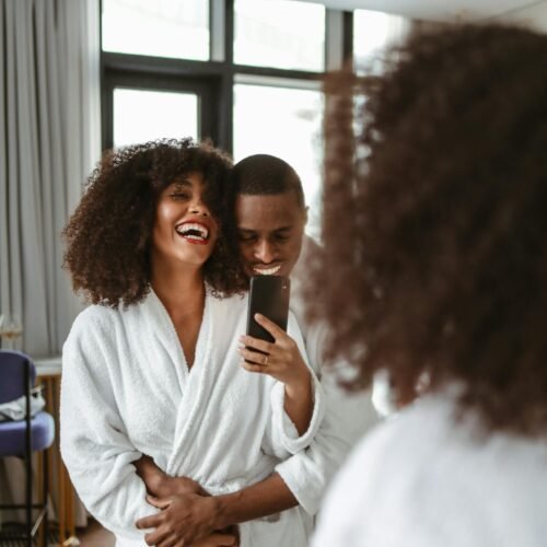 Joyful couple in bathrobes smiling and taking a selfie together indoors.
