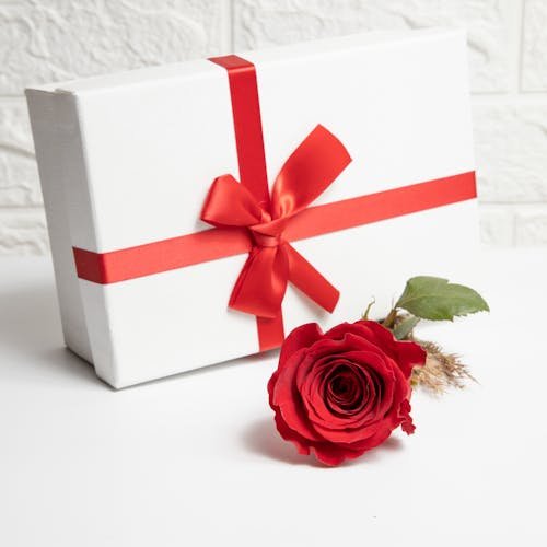 A beautifully wrapped gift box with a red bow and a red rose on a white background, perfect for celebrations.